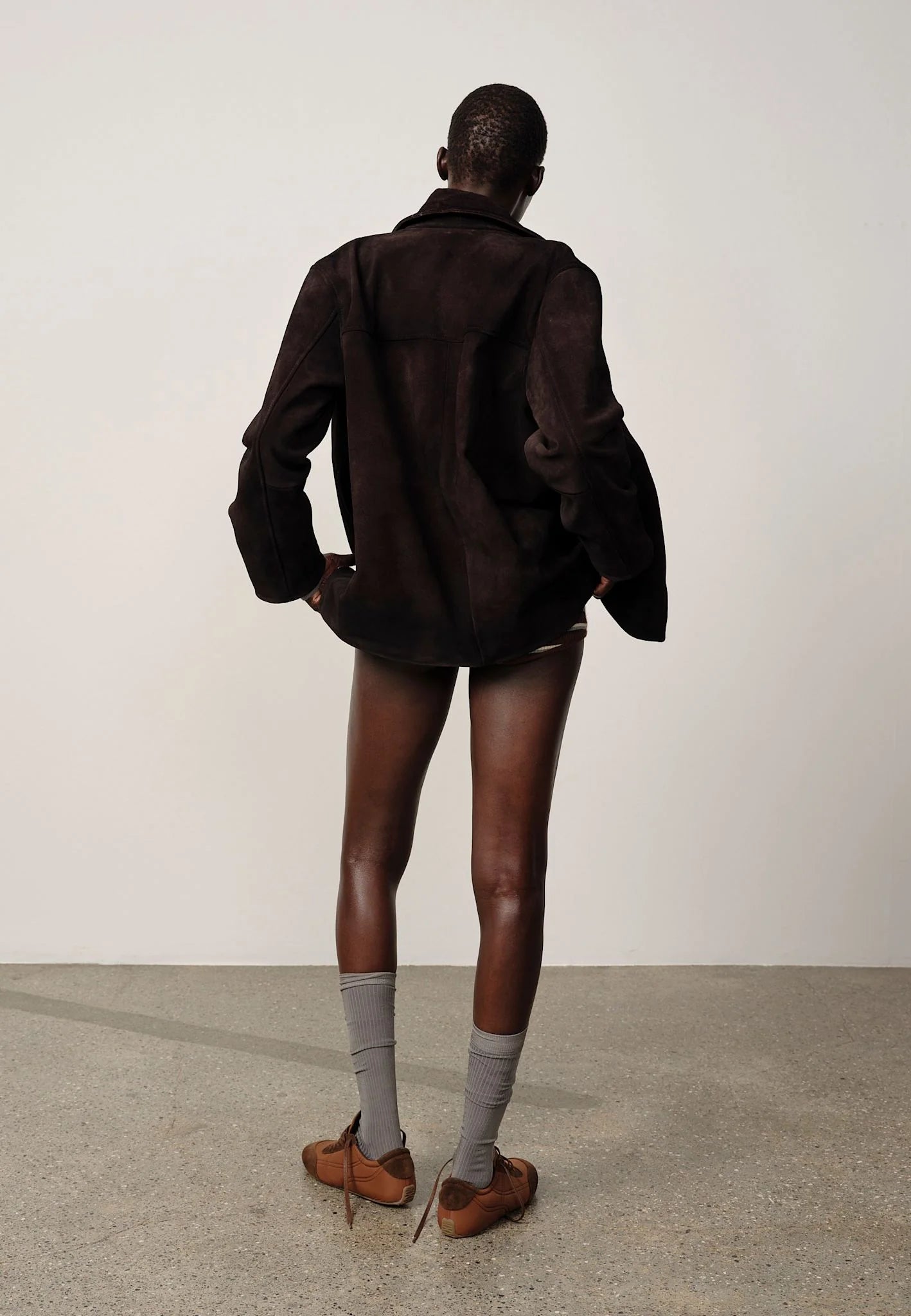 Person wearing a dark jacket, shorts, and socks standing against a plain background