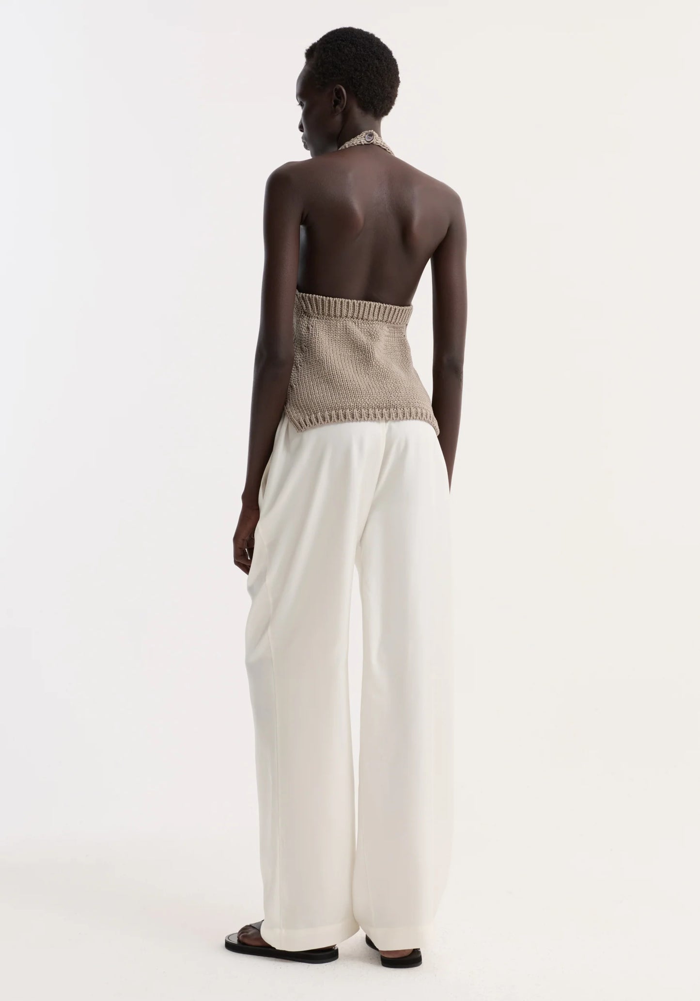 Person wearing a beige strapless top and white pants on a plain background