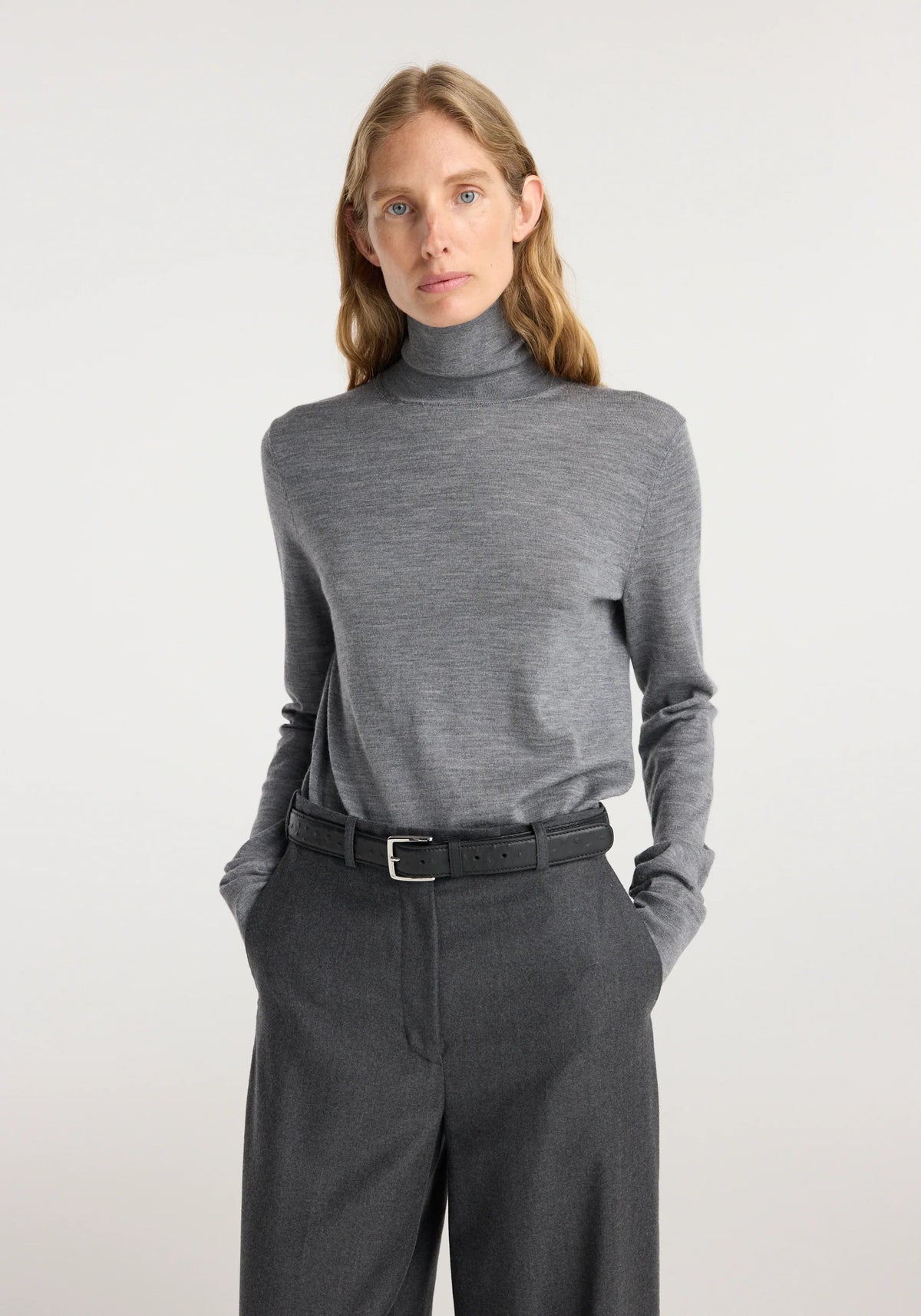 Person wearing a gray turtleneck sweater and dark pants on a light background