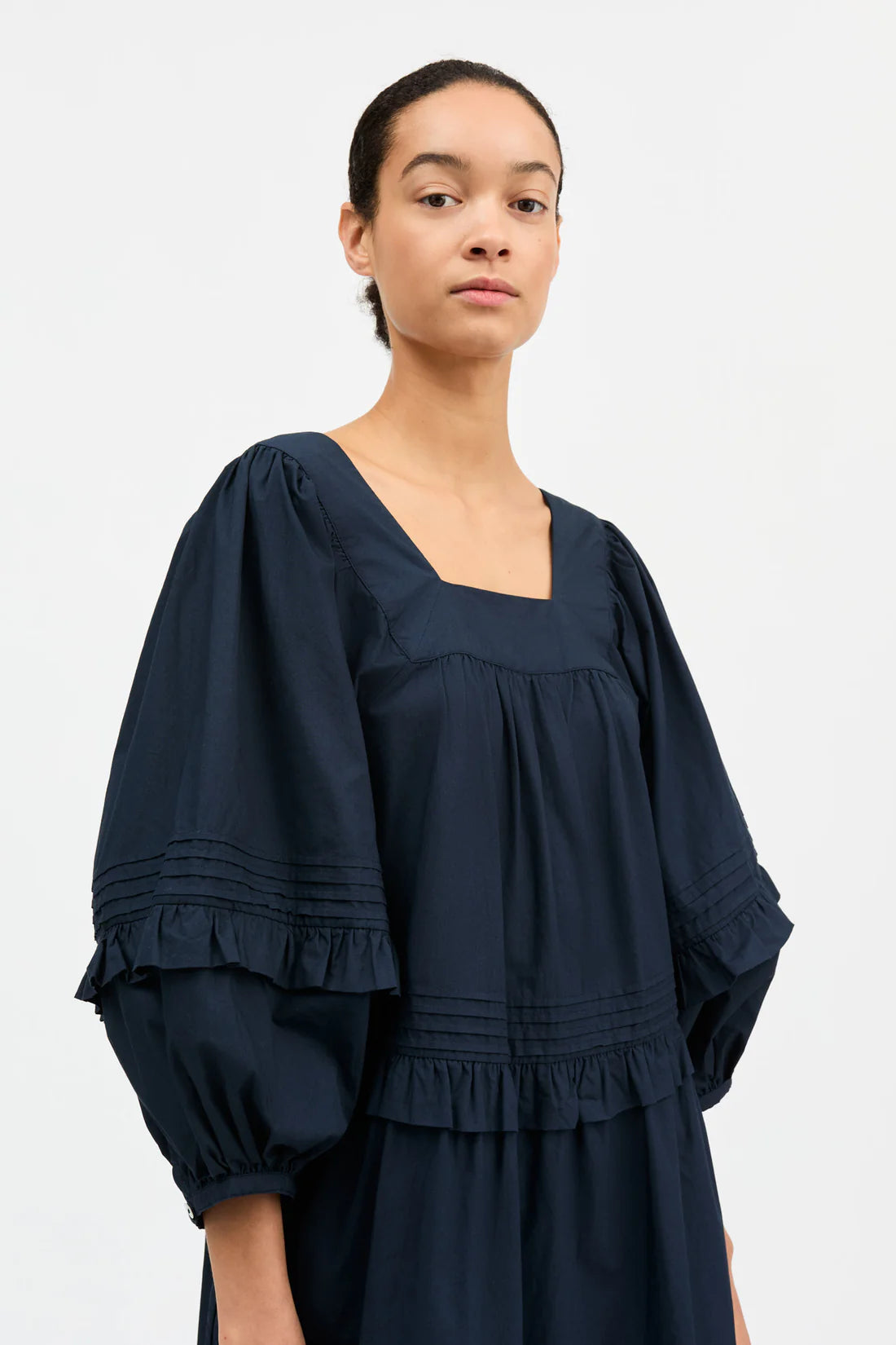 Woman wearing a navy blue dress with balloon sleeves on a white background