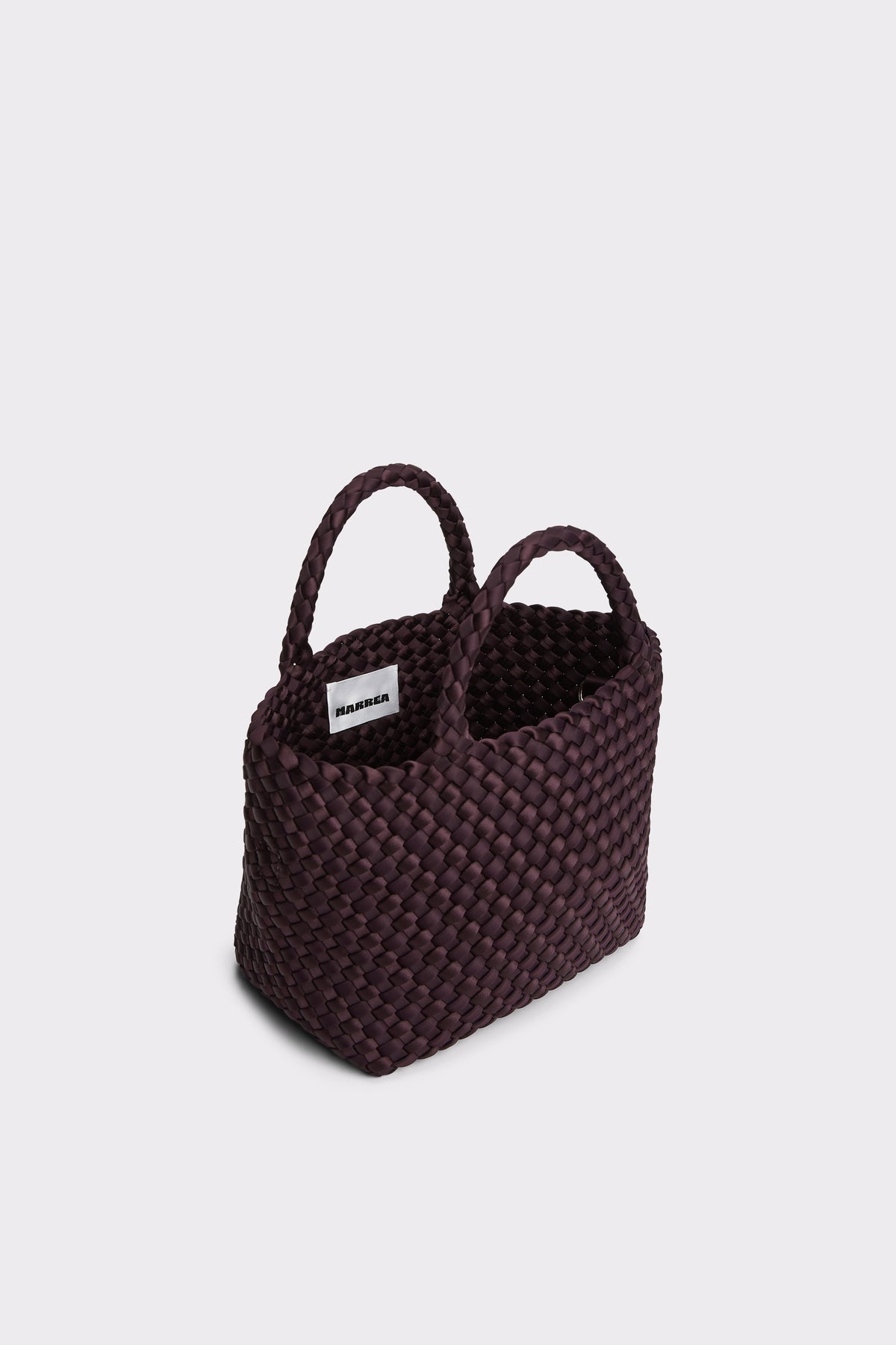 A dark plum purple woven basket bag with two top handles and a small white brand label, shown on a light gray background.