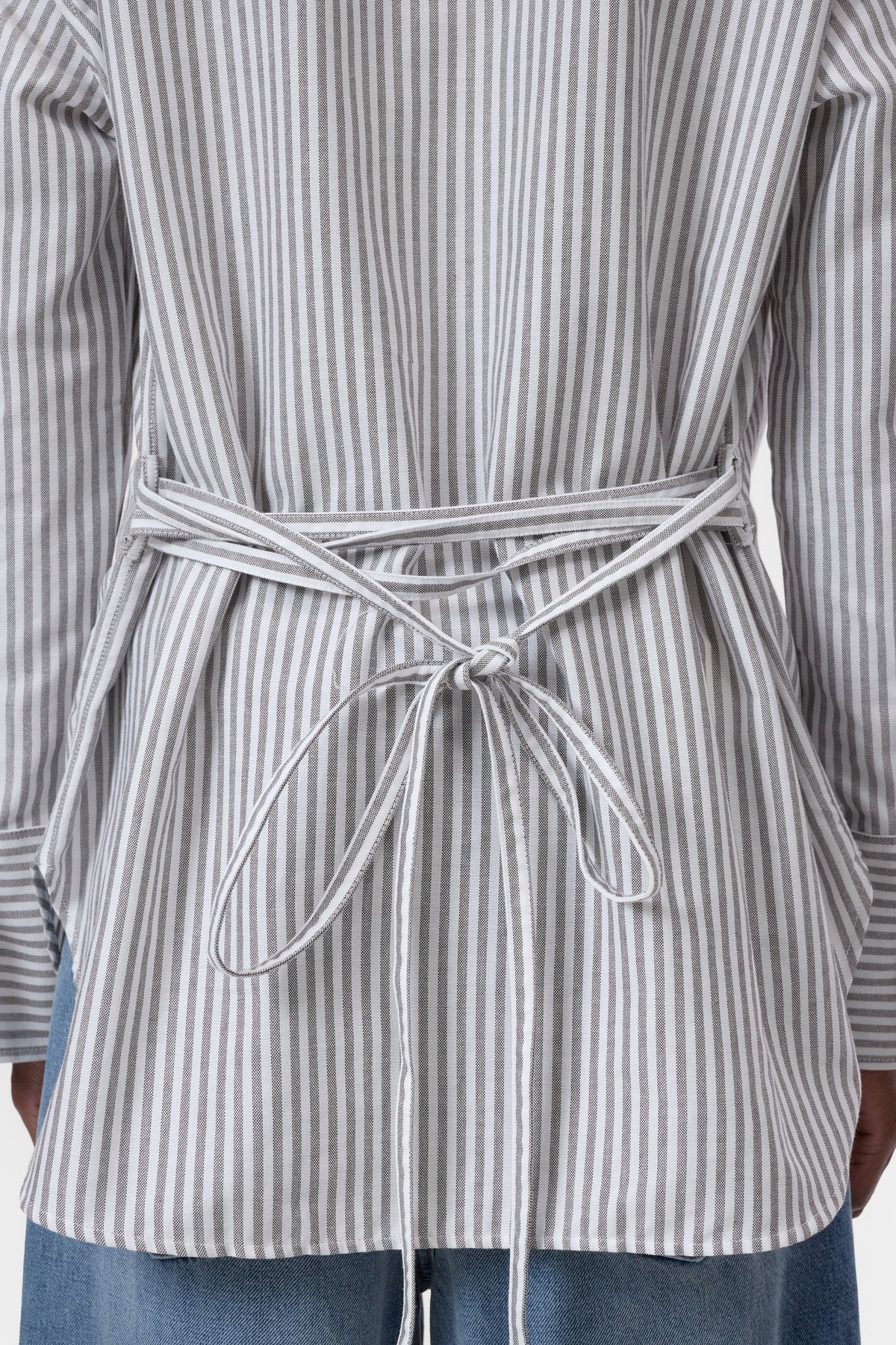 Close-up of a person wearing a gray and white vertically striped belted jacket or wrap, tied at the waist, with blue jeans visible below.