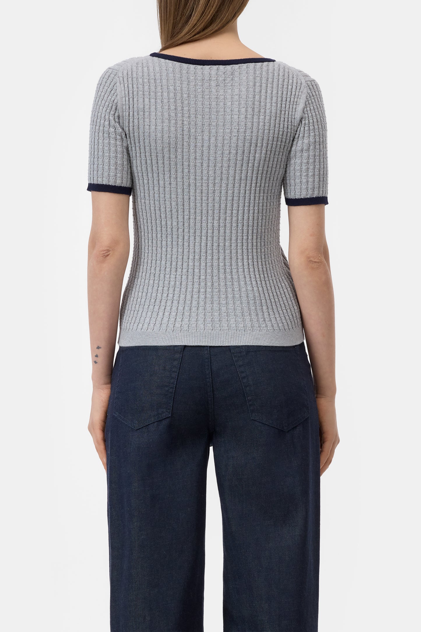 Person wearing a gray checkered top with navy trim and dark pants on a white background