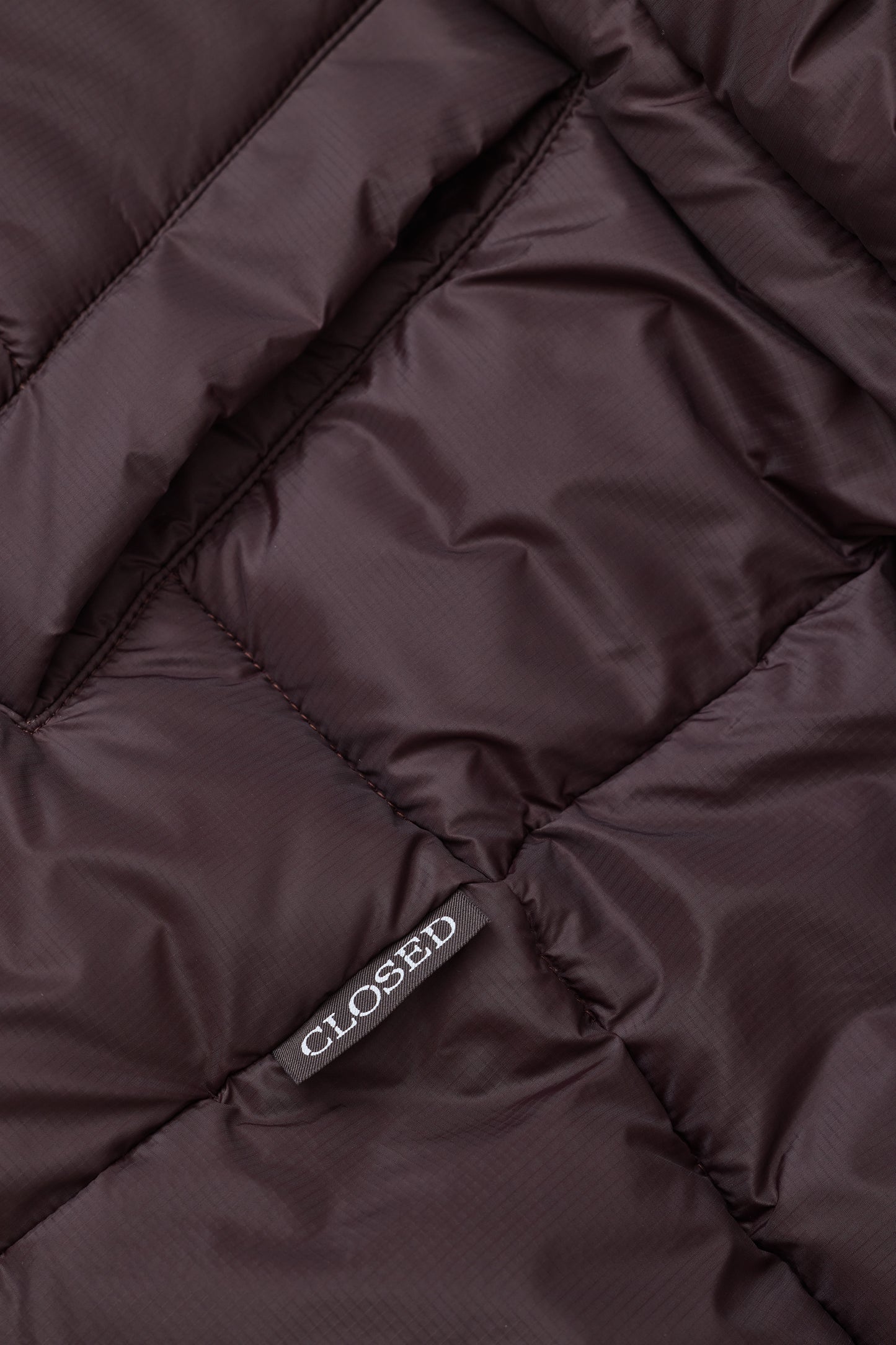 Close-up of a dark brown quilted puffer jacket fabric with a small gray tag reading 'CLOSED'.