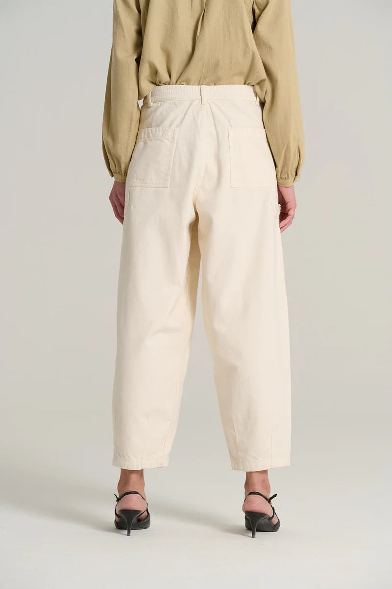 A person shown from the back wearing cream-colored wide-leg cropped trousers, a beige long-sleeve top, and black pointed-toe heeled sandals against a light gray studio background.