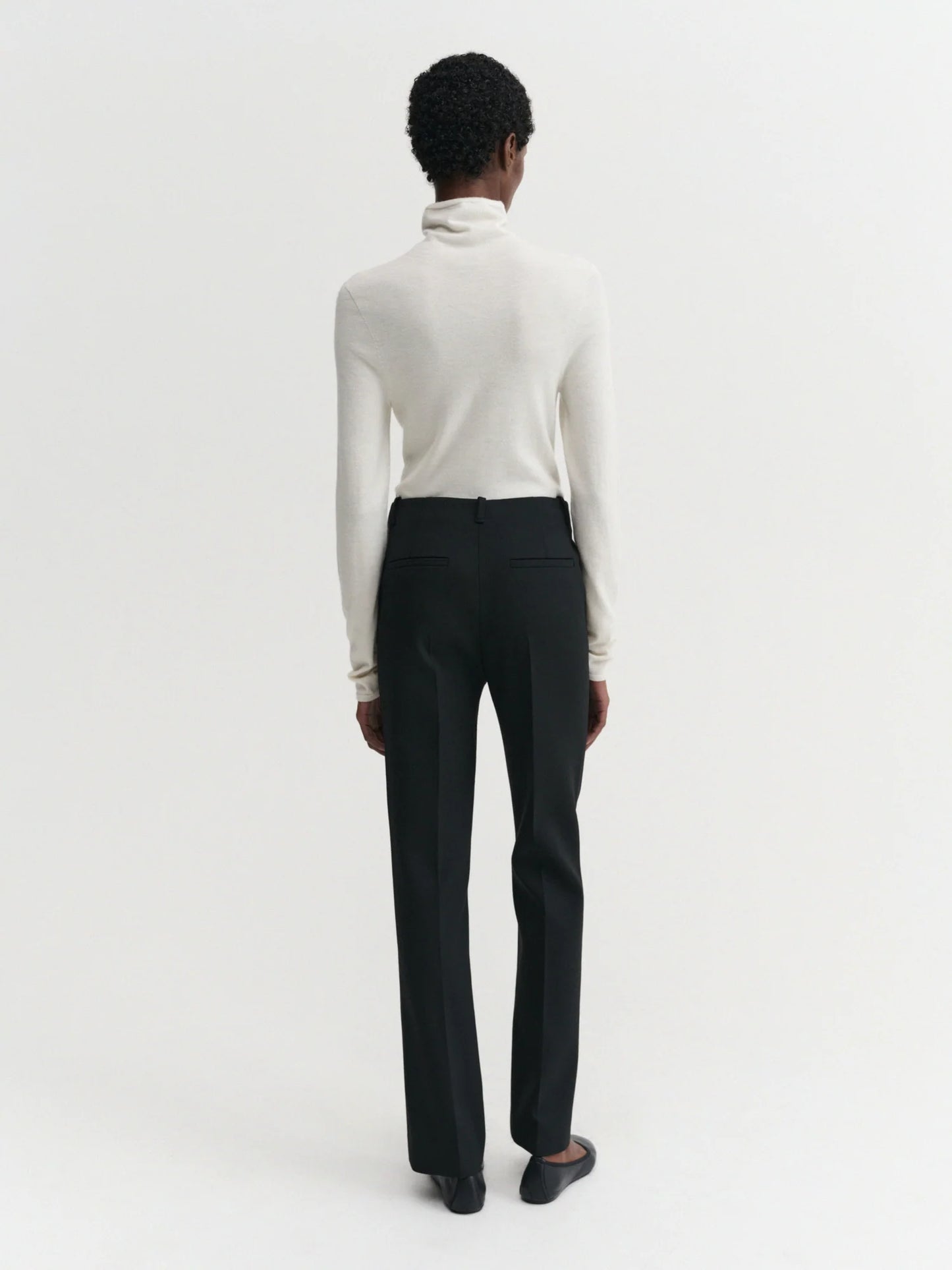 Person wearing a white turtleneck and black pants on a white background