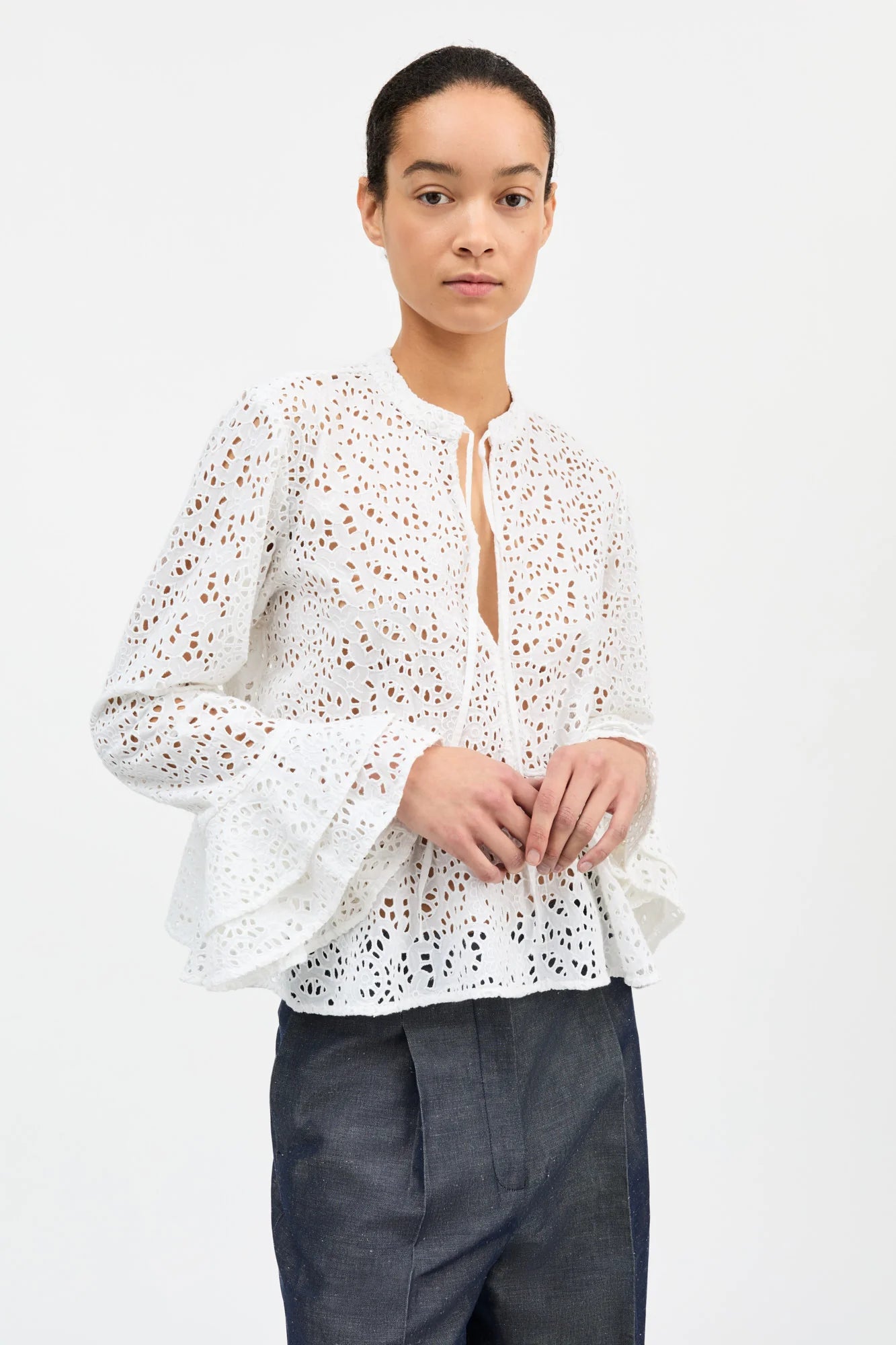 Woman wearing a white lace blouse with dark pants on a light background