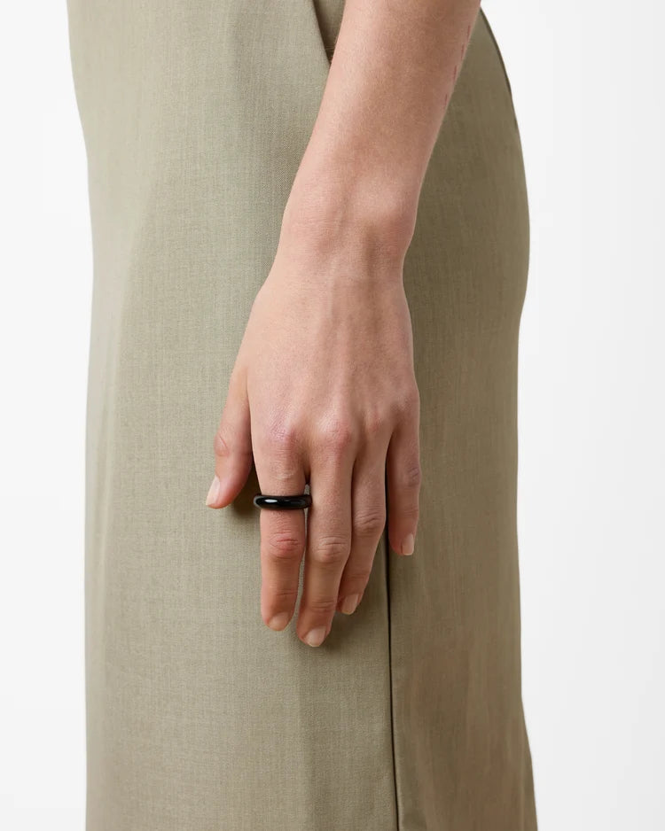 A close-up of a person's hand wearing a simple black band ring, shown against a light neutral background.