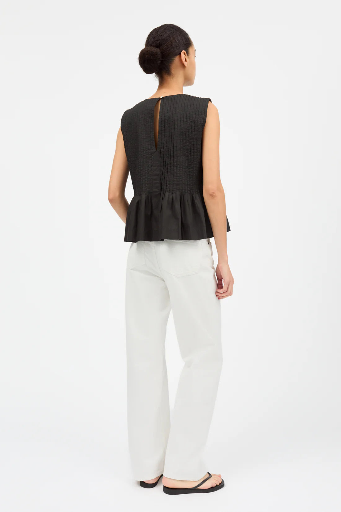 Woman wearing a black sleeveless peplum top and white pants on a white background