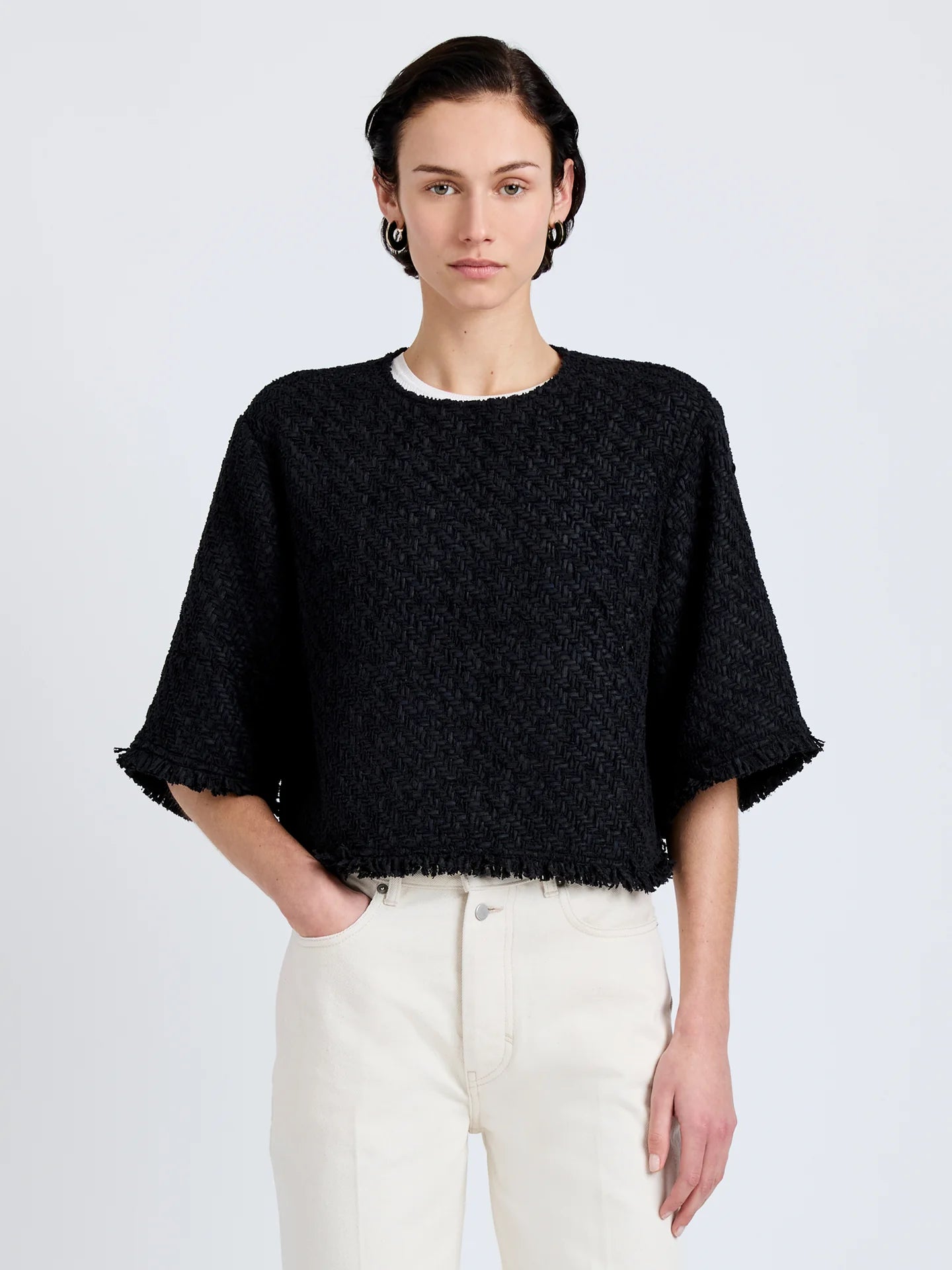 Person wearing a black textured sweater and white pants on a light gray background