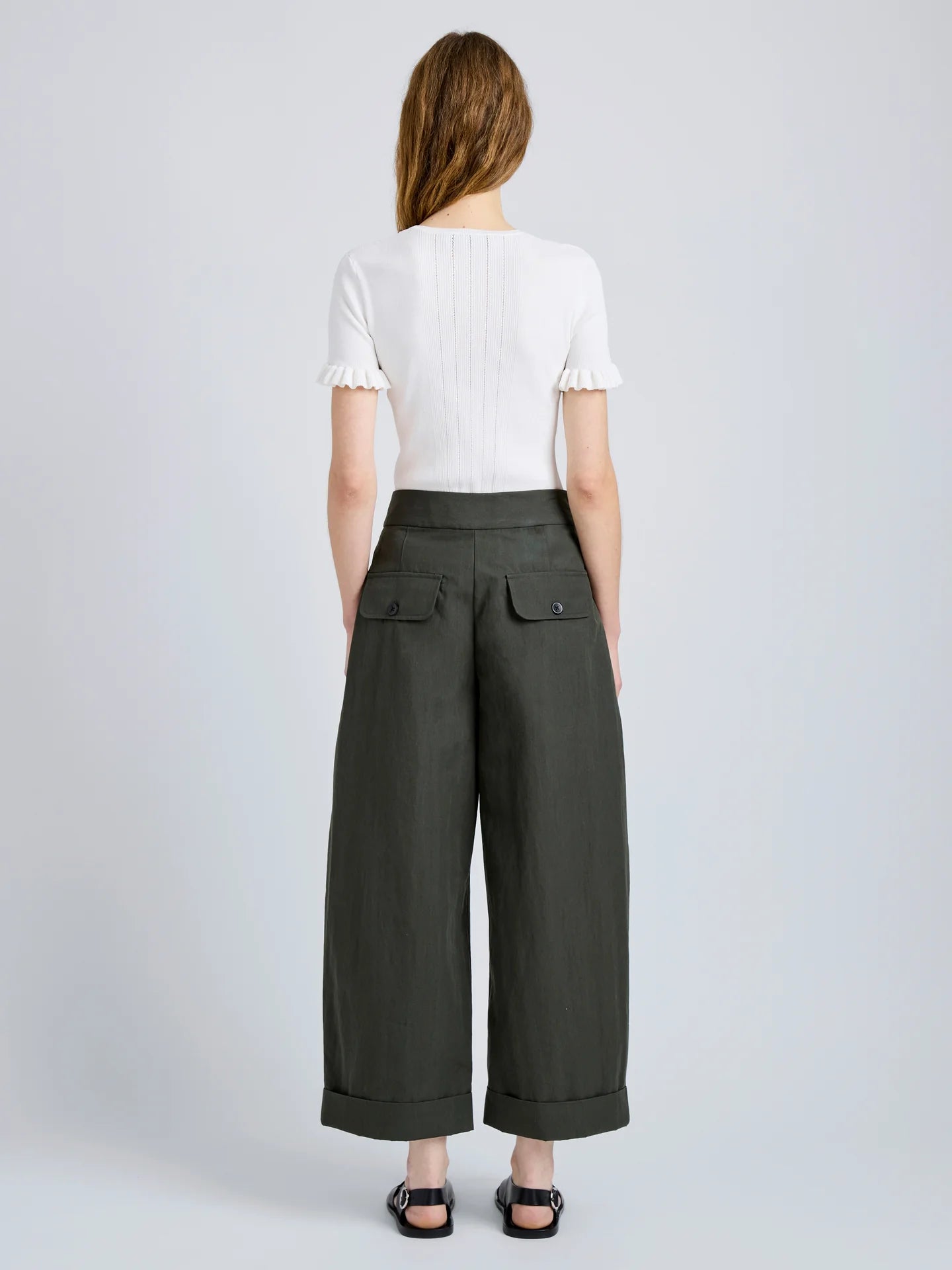 Person wearing a white top and dark green wide-leg pants on a light gray background