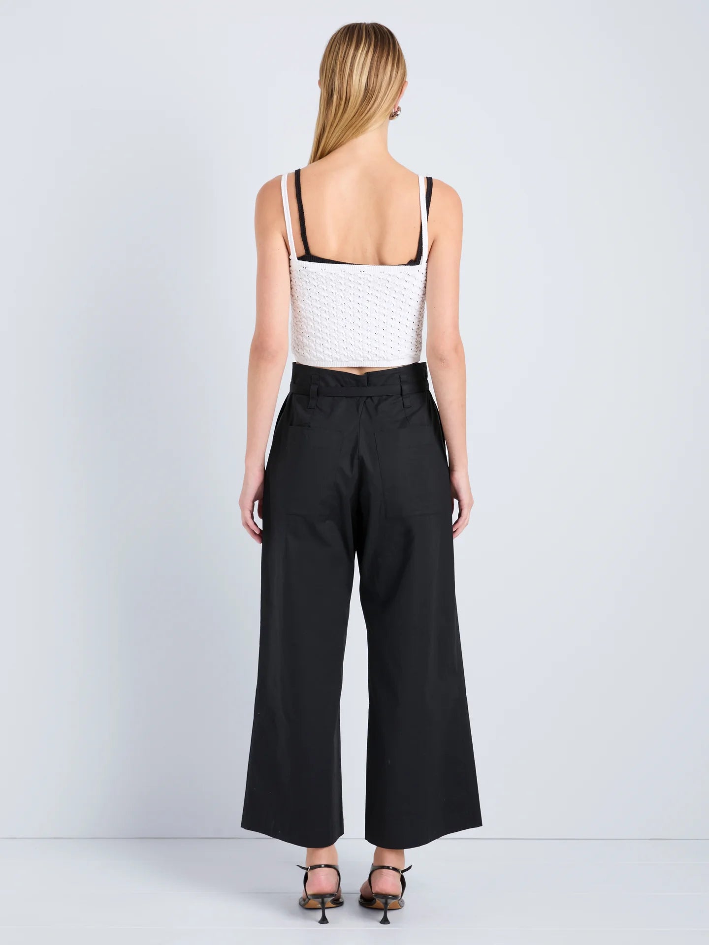 Woman wearing a white top and black wide-leg pants on a light gray background