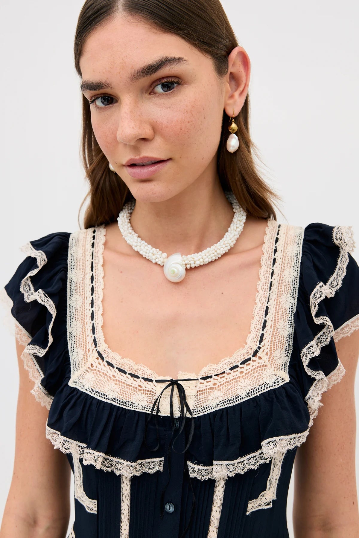 Woman wearing a navy dress with lace details and a pearl necklace on a white background