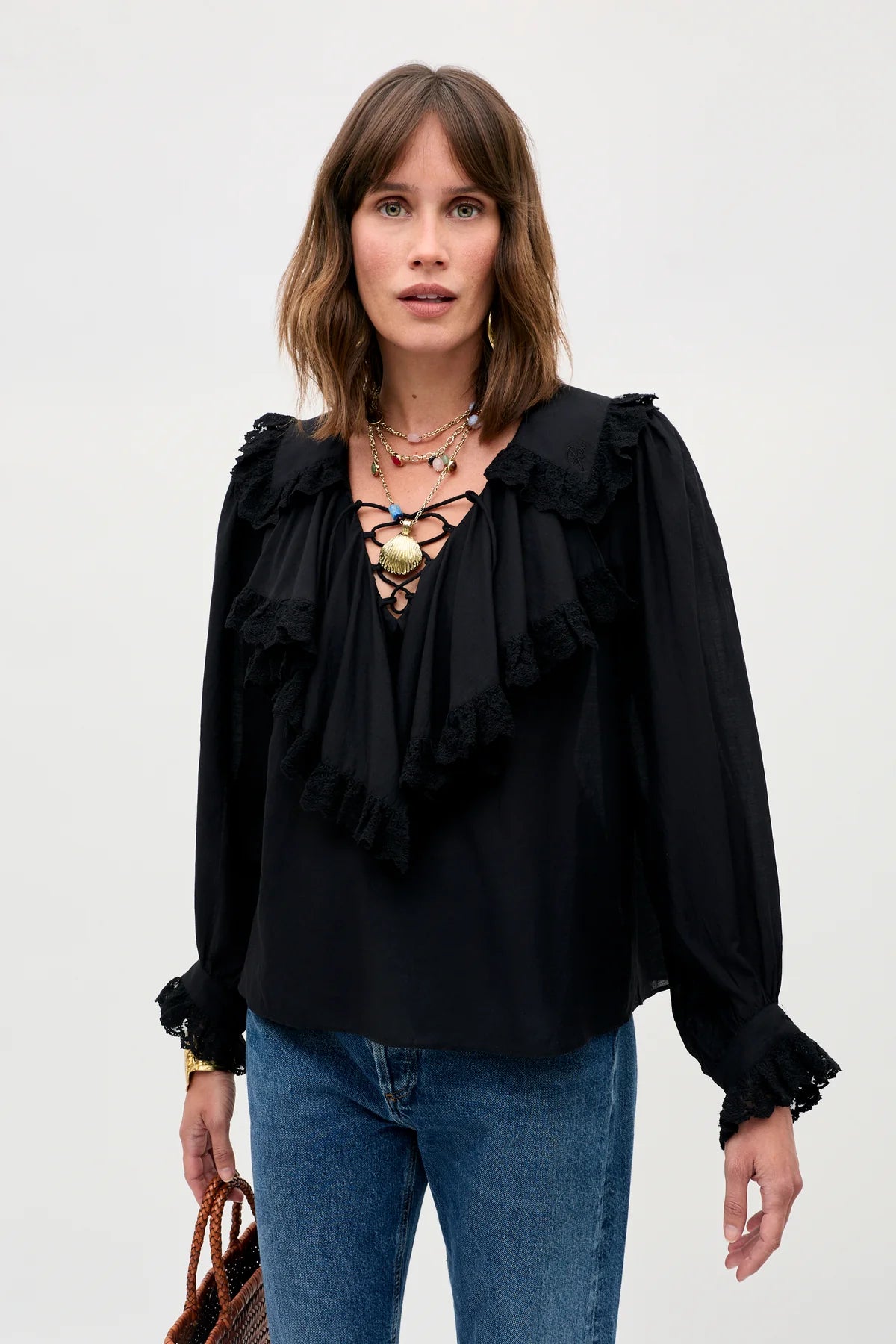 Woman wearing a black blouse with ruffles and blue jeans on a white background