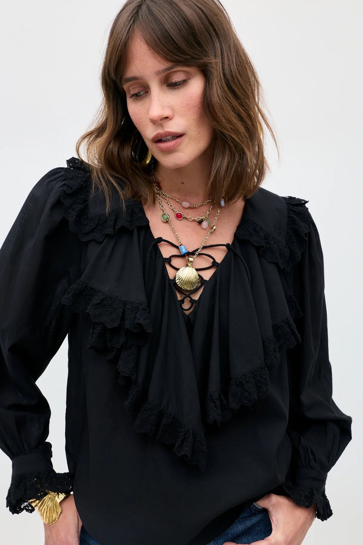 Woman wearing a black blouse with ruffled details and layered necklaces on a white background