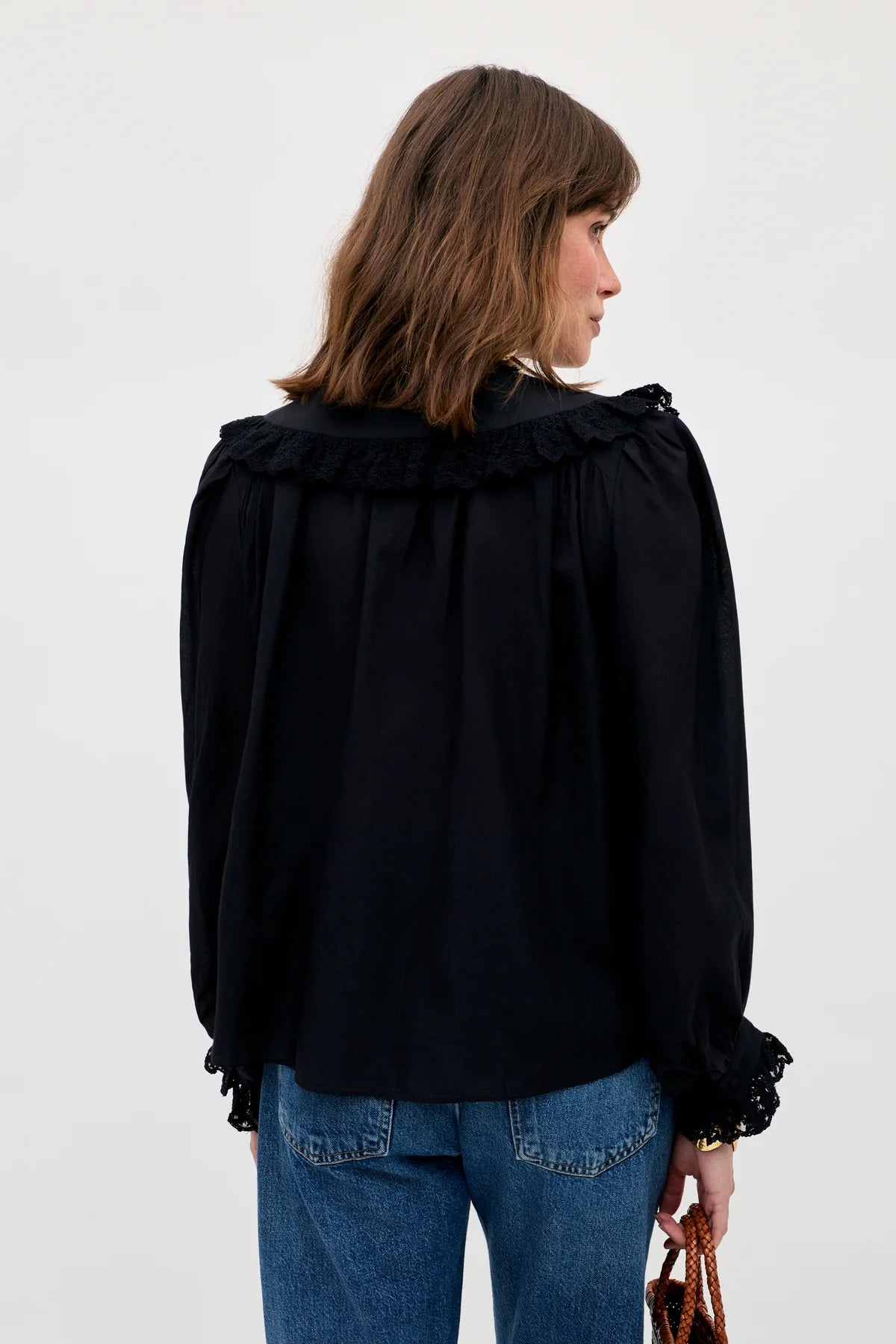 Woman wearing a black blouse with ruffled sleeves and blue jeans on a white background