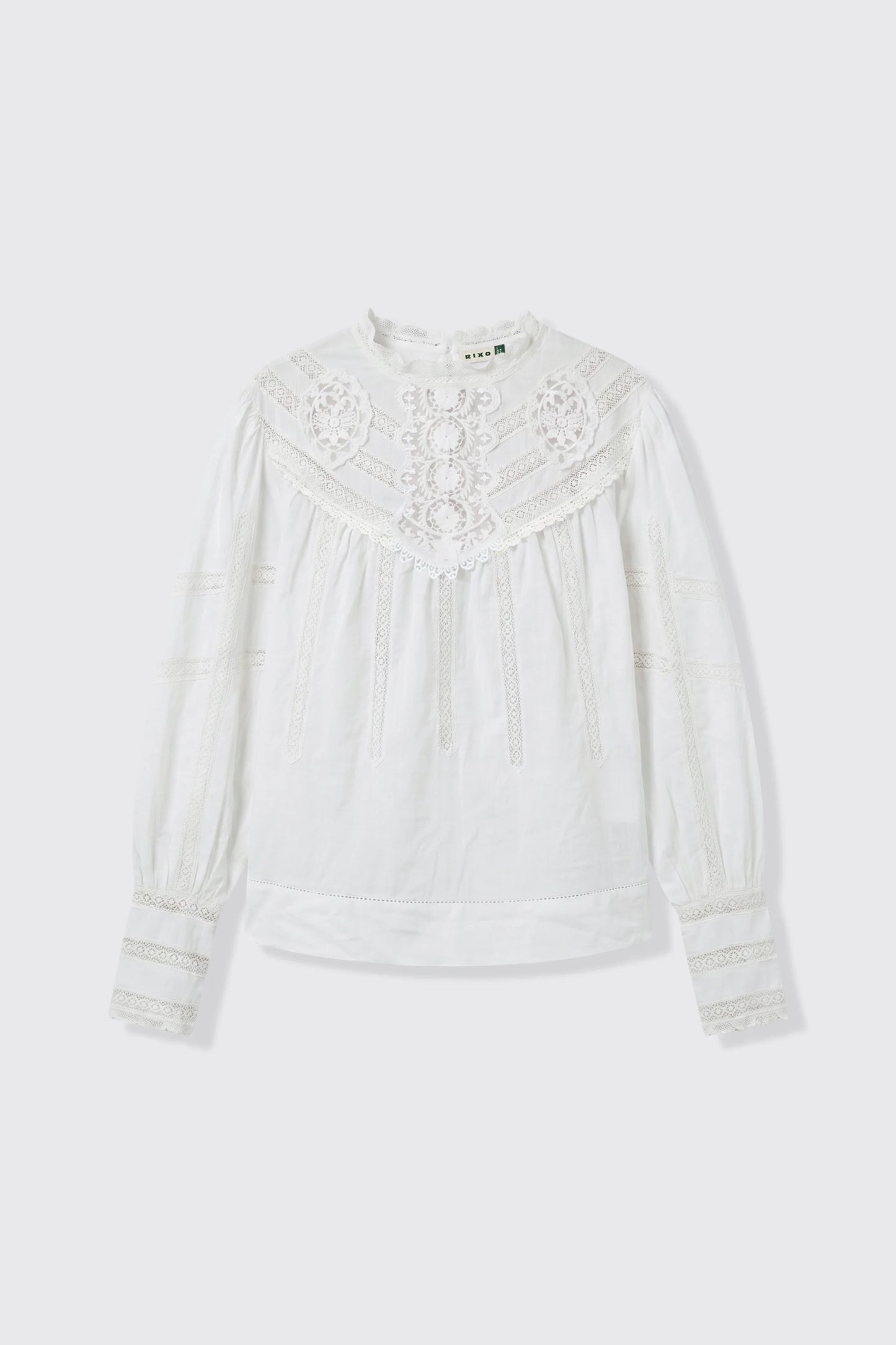 A white long-sleeve blouse with intricate lace and embroidery on the yoke and cuffs, displayed flat against a light gray background.