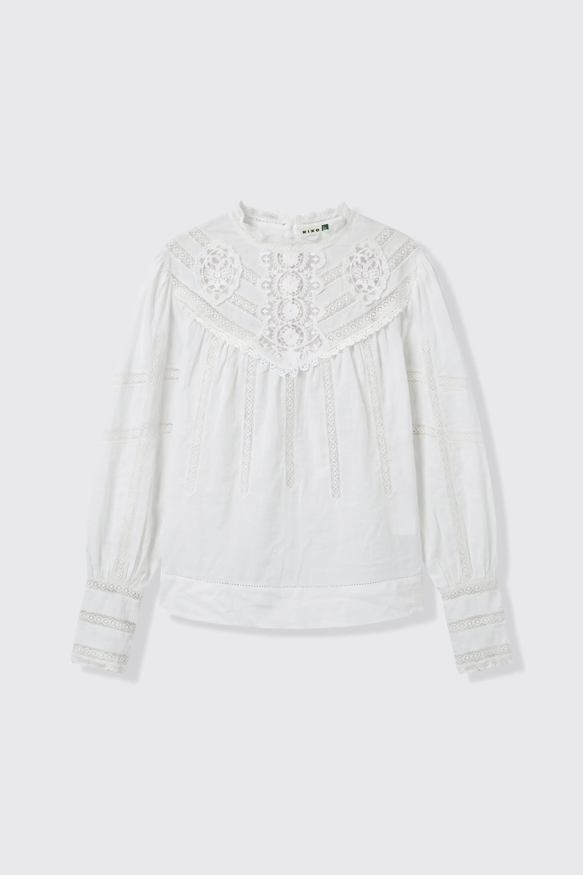 A white long-sleeve blouse with intricate lace and embroidery on the yoke and cuffs, displayed flat against a light gray background.