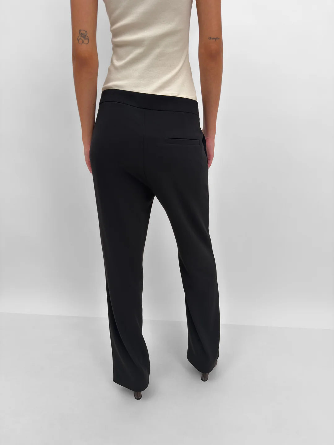 Person wearing black pants and a beige top on a white background