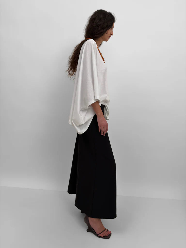 Woman wearing a white top and black skirt on a plain background