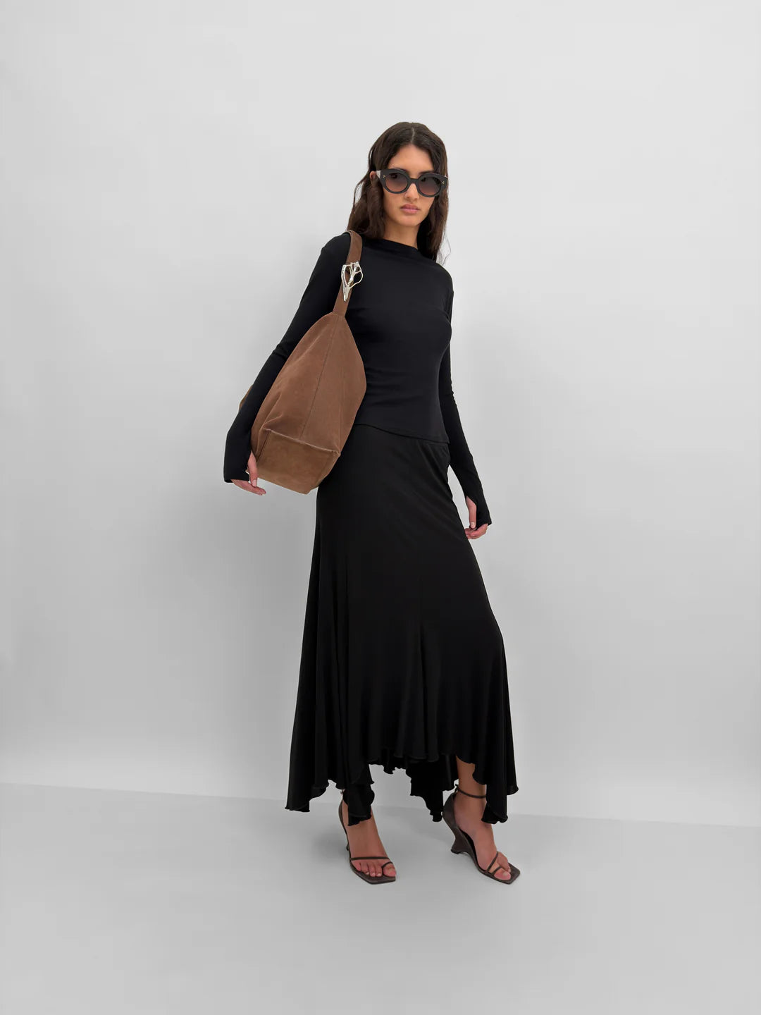 Woman in a black outfit holding a brown bag against a white background