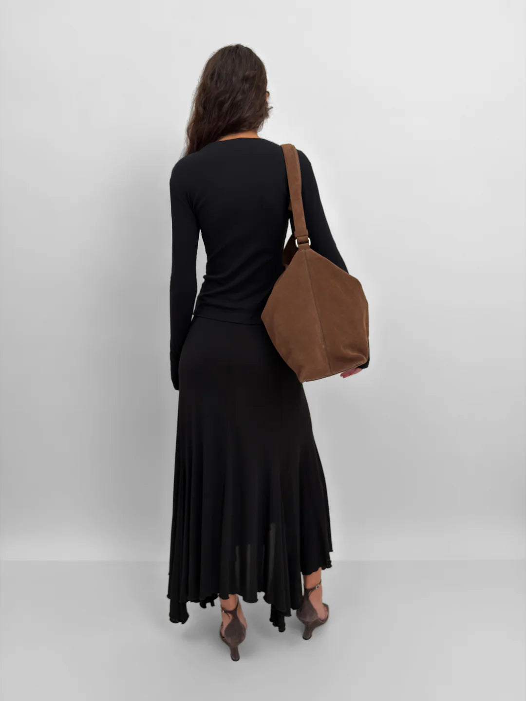Woman in a black dress holding a brown bag against a white background