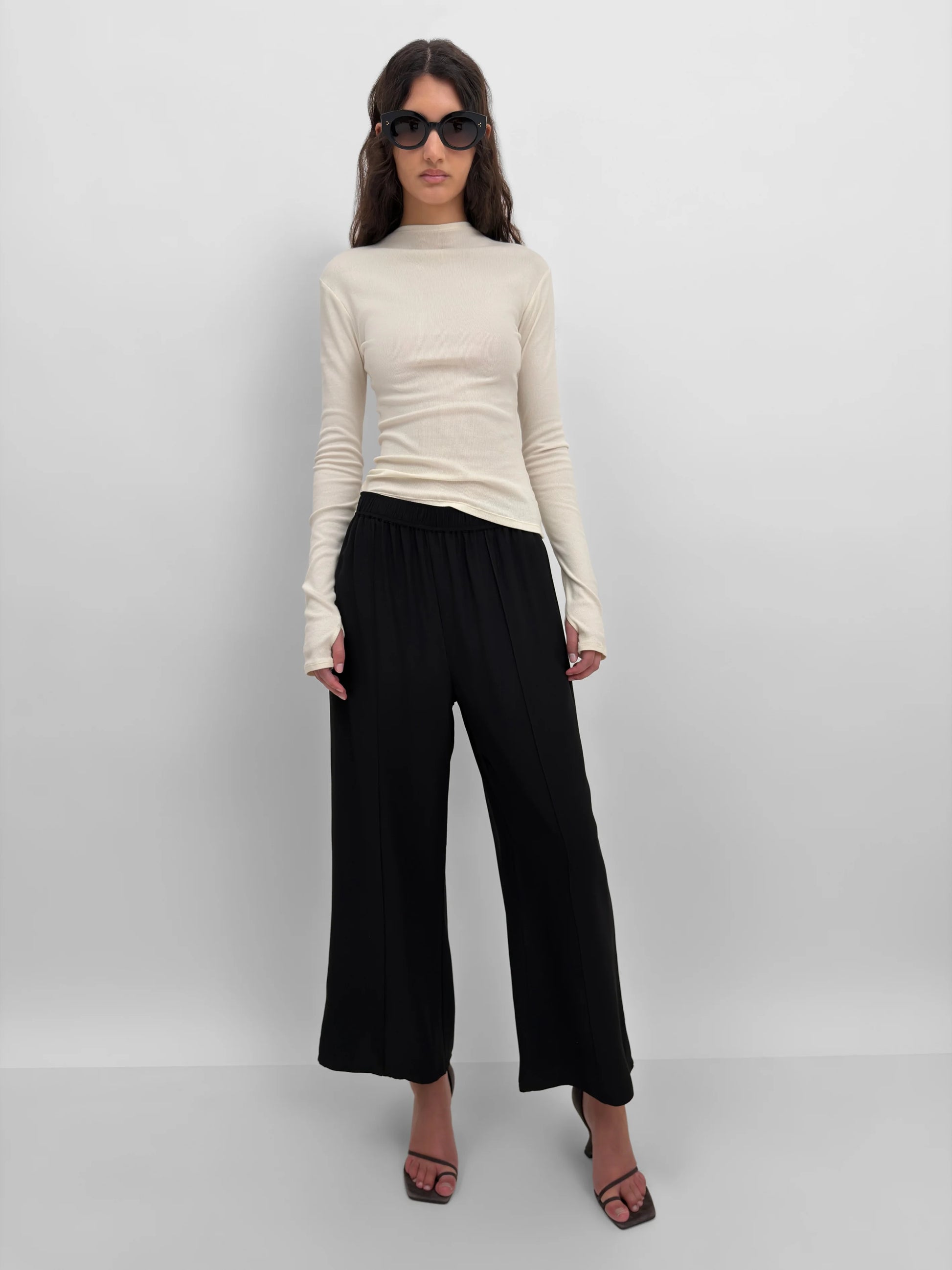 Woman wearing a beige long-sleeve top and black wide-leg pants on a white background