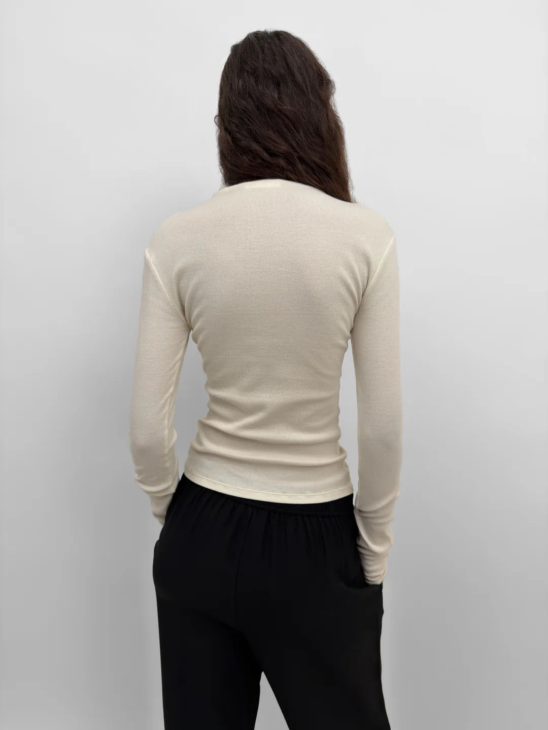 Person wearing a beige long-sleeve top and black pants against a plain background