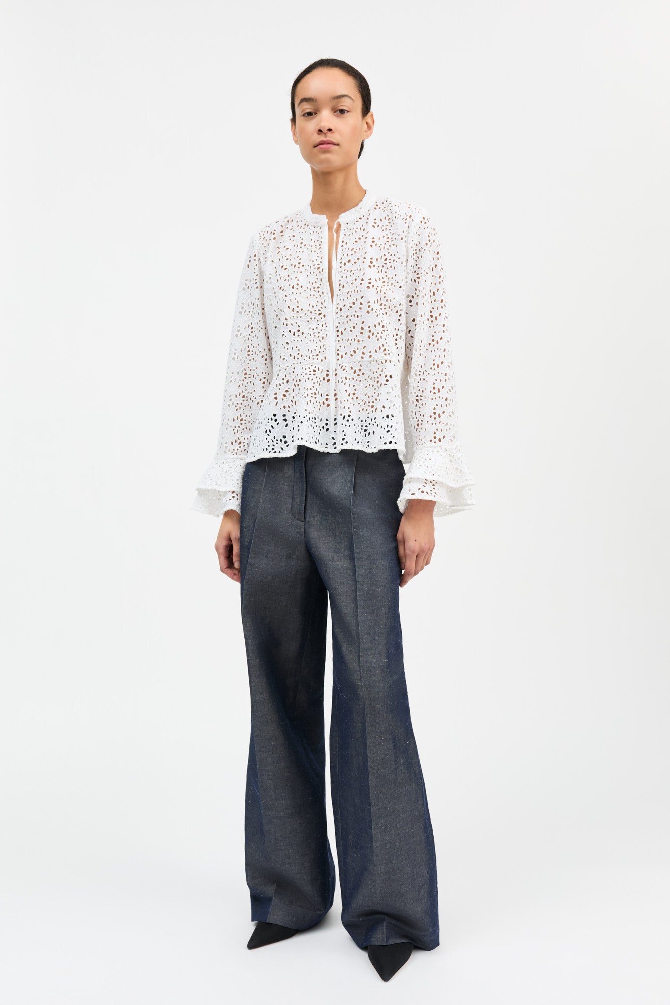 Person wearing a white lace blouse and dark pants on a white background
