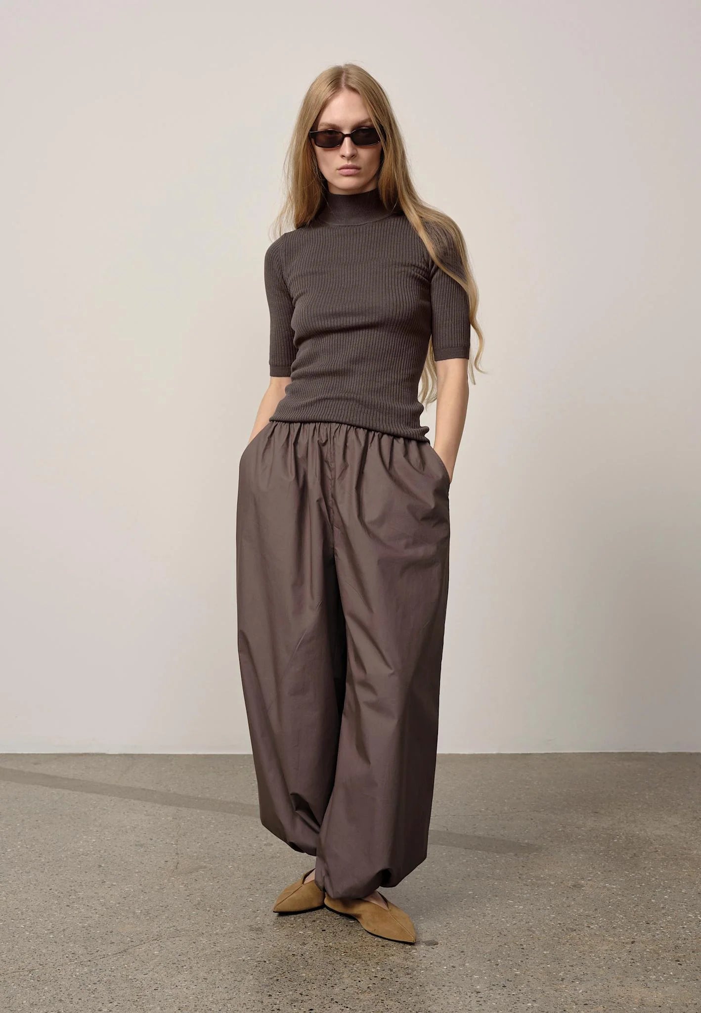 Woman wearing a brown turtleneck and wide-leg pants against a plain background