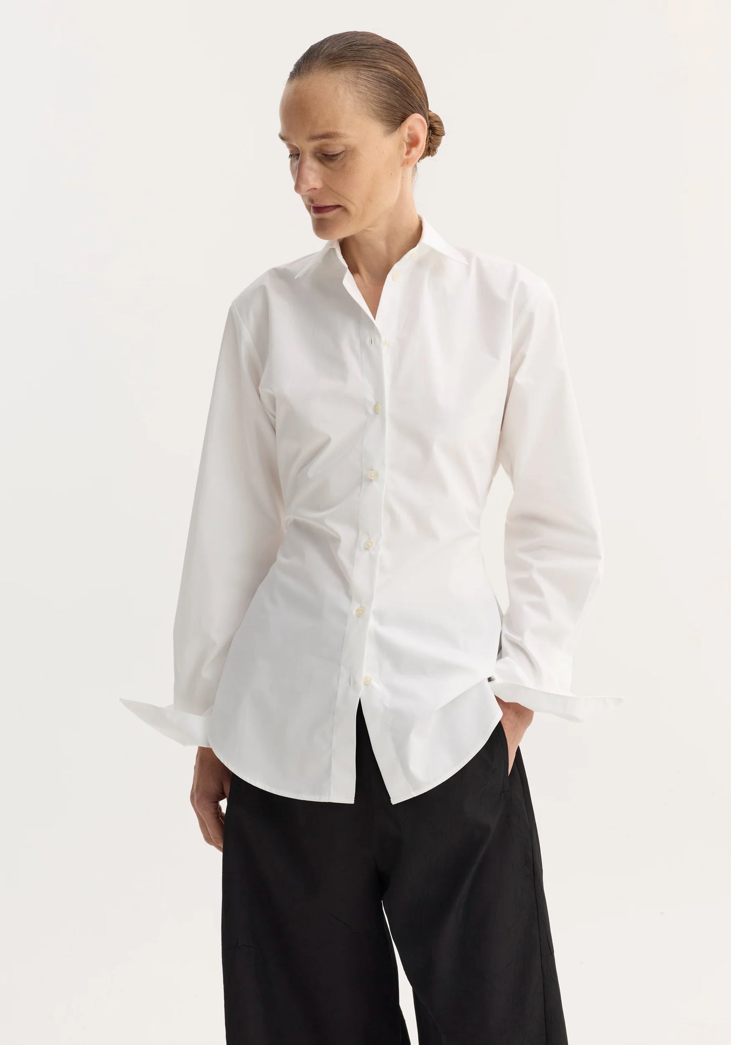 Woman wearing a white shirt and black pants on a plain background