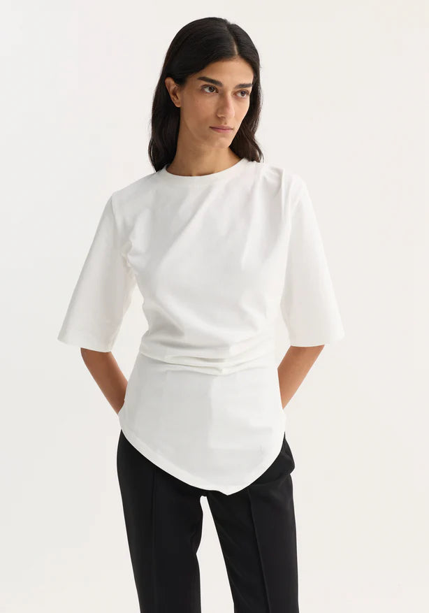 Woman wearing a white blouse with a subtle pattern on a plain background