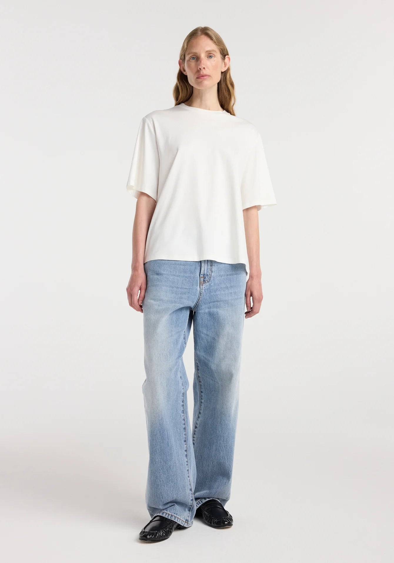 Person wearing a white t-shirt and blue jeans on a plain background