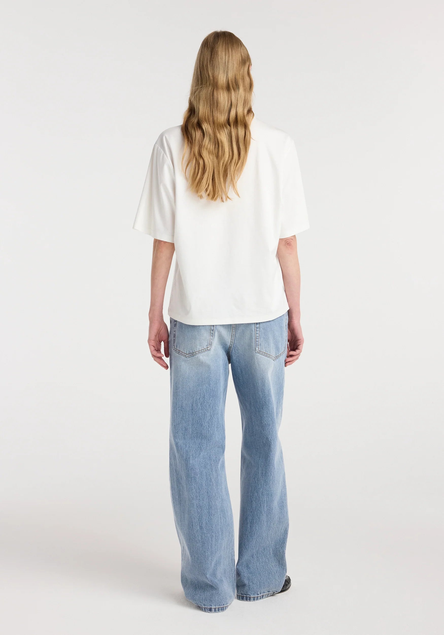 Person wearing a white top and light blue jeans on a white background