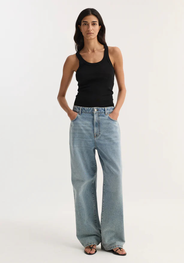 Woman wearing a black tank top and light blue jeans on a white background