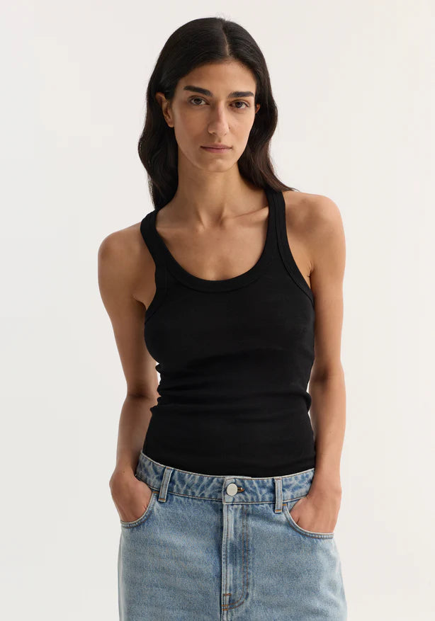 Woman wearing a black tank top and blue jeans against a white background