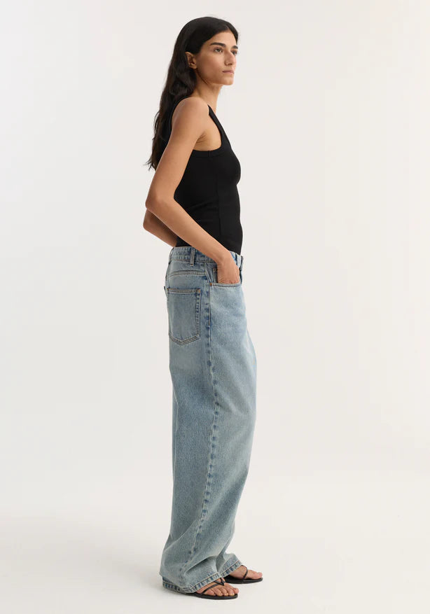 Woman wearing a black tank top and light blue jeans on a white background