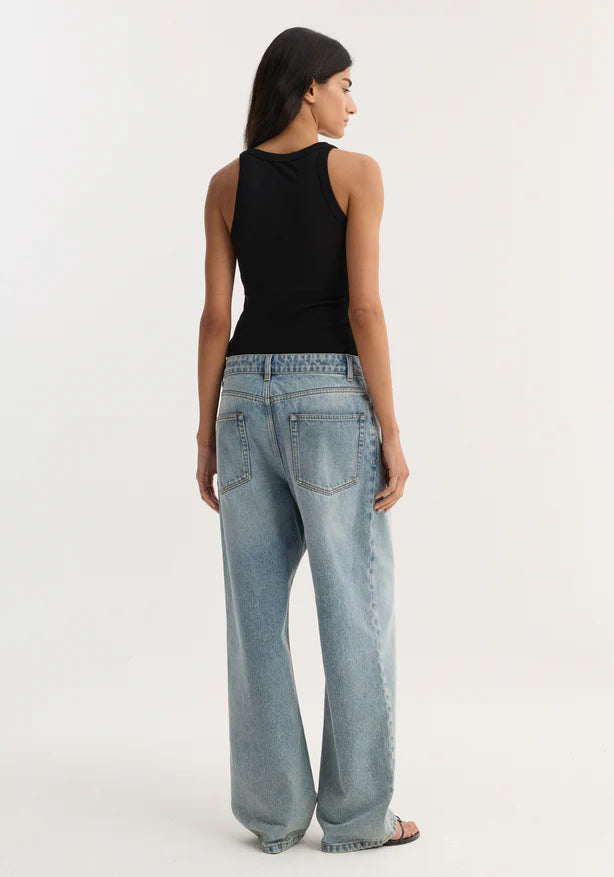 Woman wearing light blue jeans and a black sleeveless top on a white background
