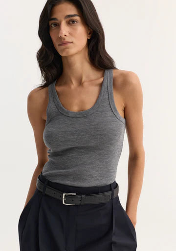A woman wearing a heather gray ribbed tank top and dark navy trousers with a black belt, photographed against a plain light background.