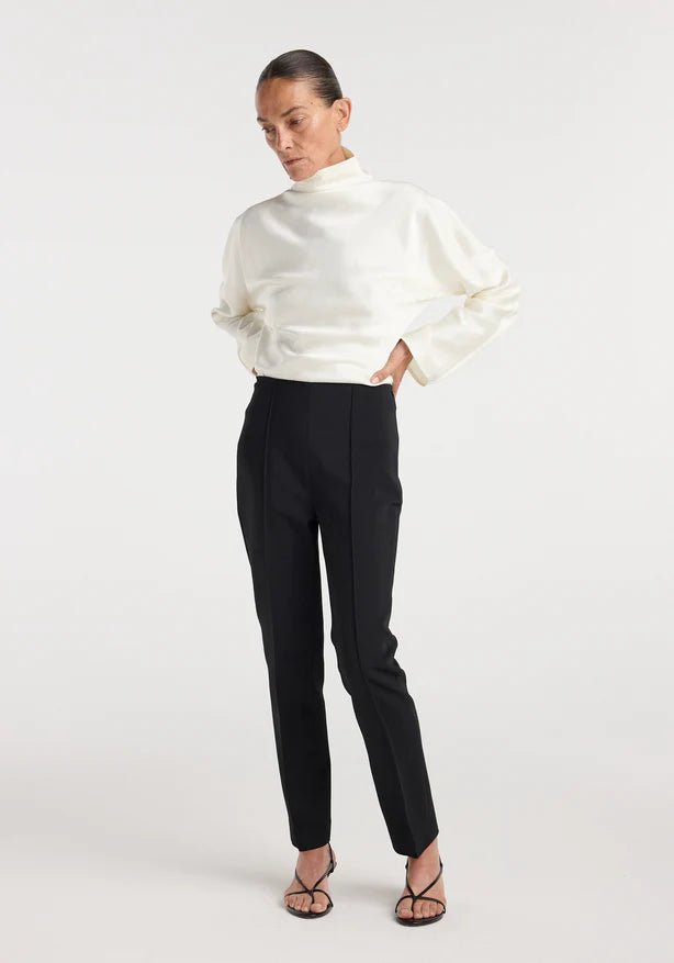 Woman wearing a white turtleneck sweater and black pants on a white background