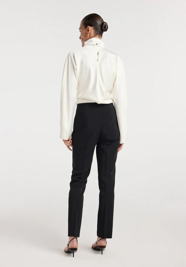 Person wearing a white blouse and black pants on a plain background