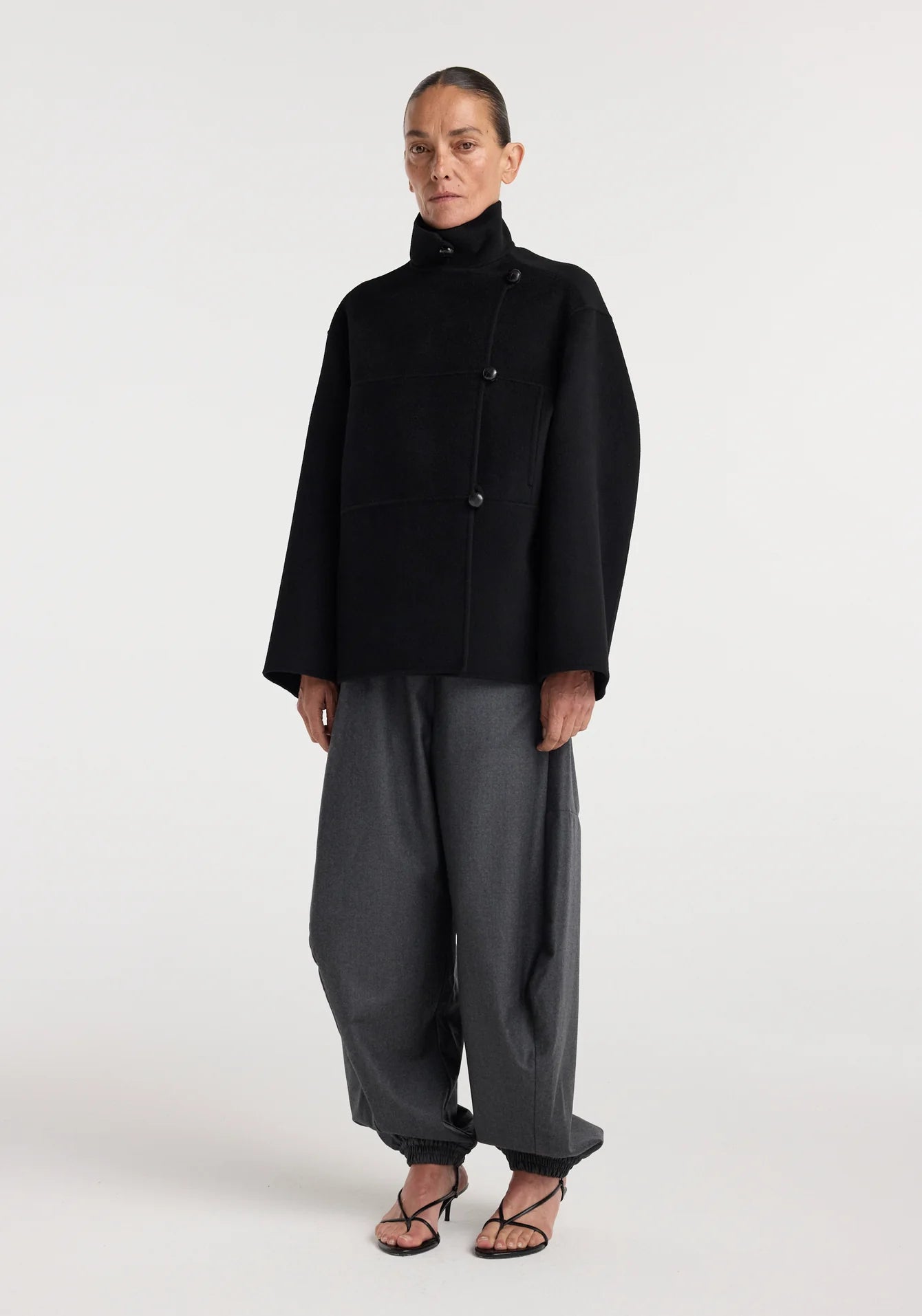 Person wearing a black coat and gray pants on a white background