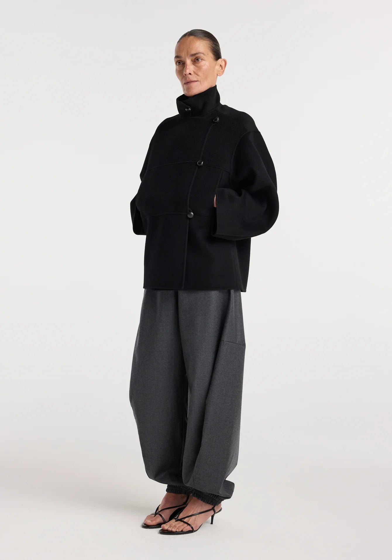 Person wearing a black coat and gray pants on a white background