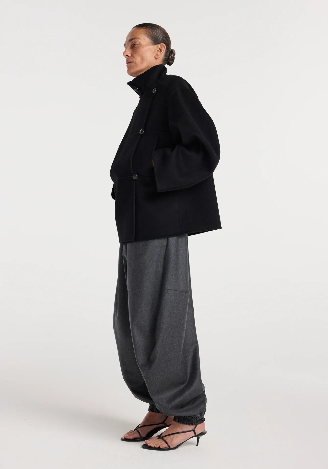 Person wearing a black coat and gray pants on a white background