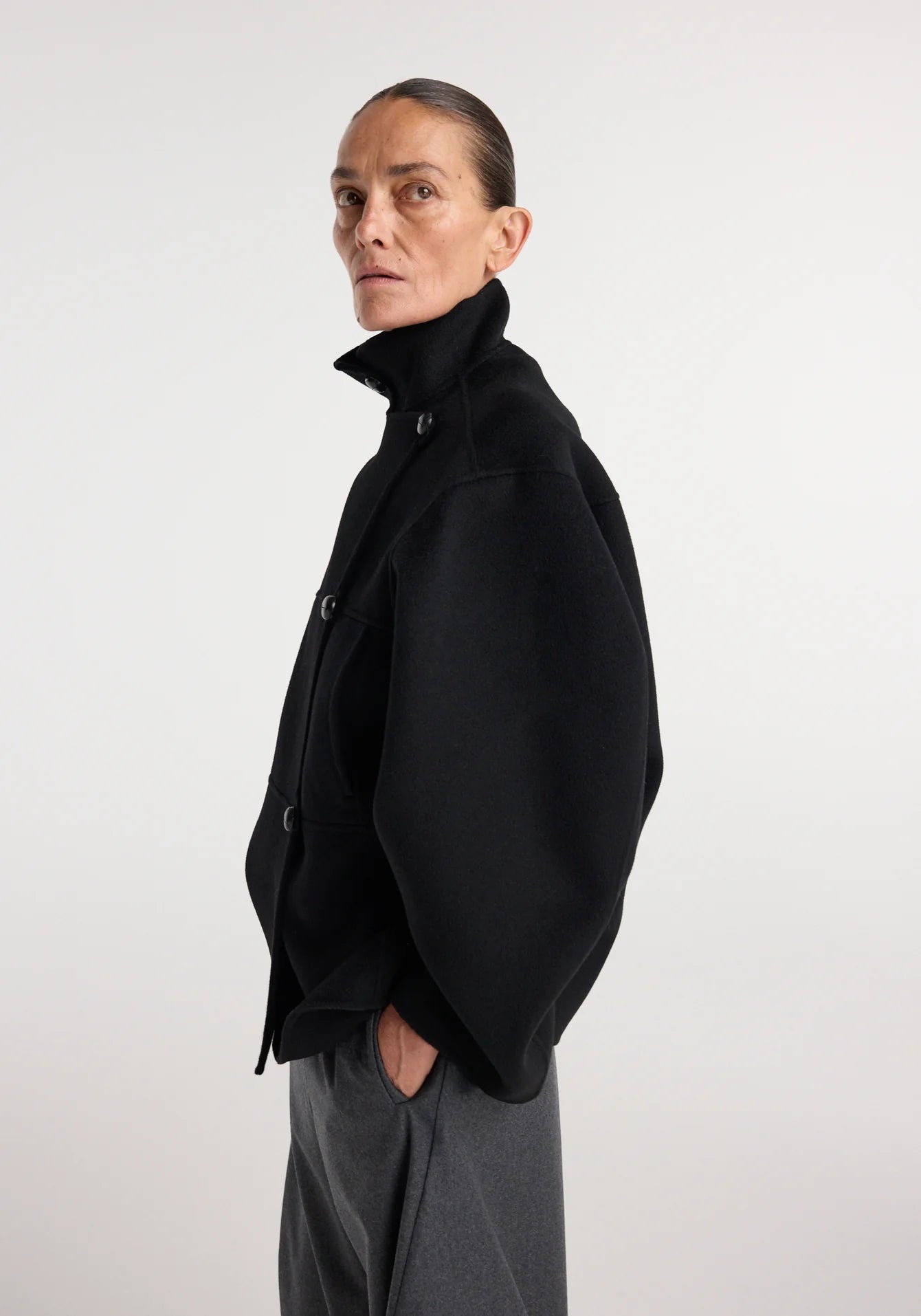 Person wearing a black coat and gray pants on a white background