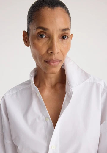 A close-up portrait of a model wearing a white button-down shirt against a plain light background.
