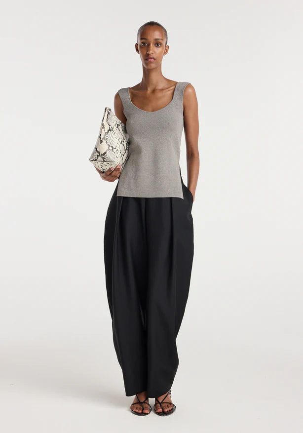 Woman wearing a gray tank top and black pants holding a patterned bag on a white background