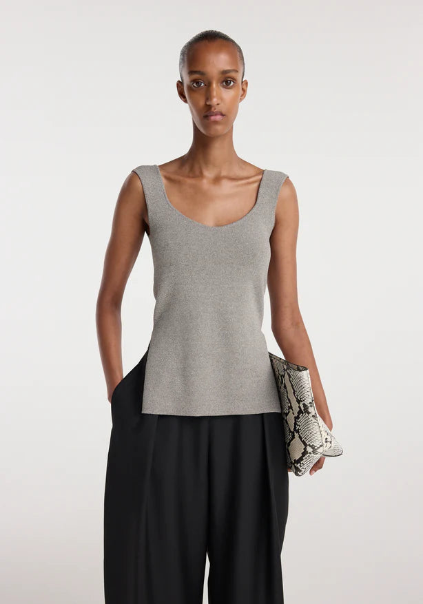 Woman wearing a gray tank top and black pants, holding a clutch against a white background