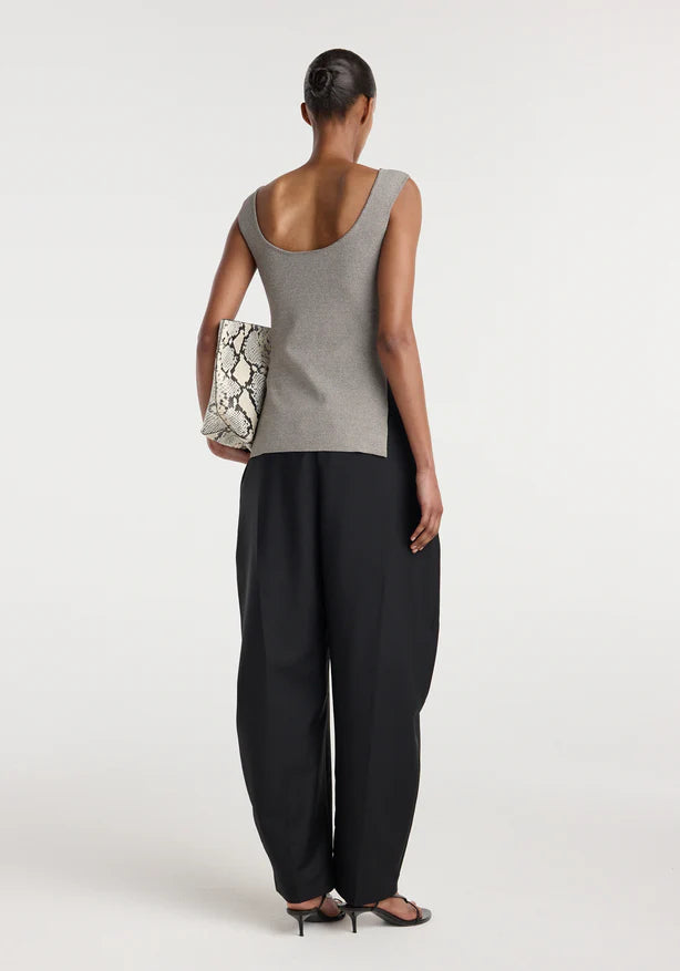 Woman wearing a gray sleeveless top and black pants, holding a clutch, on a white background