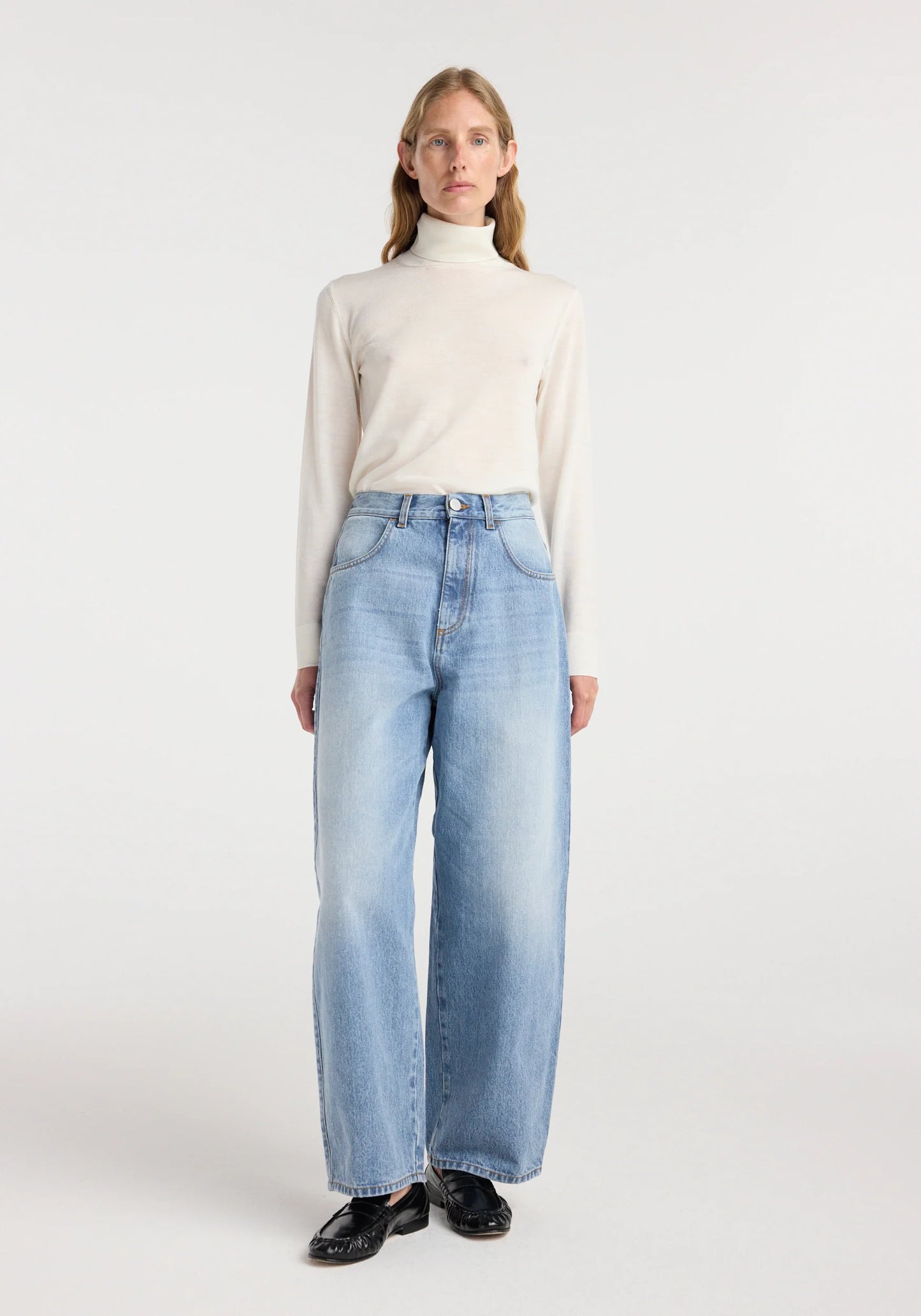 Woman wearing a white turtleneck and light blue jeans on a white background